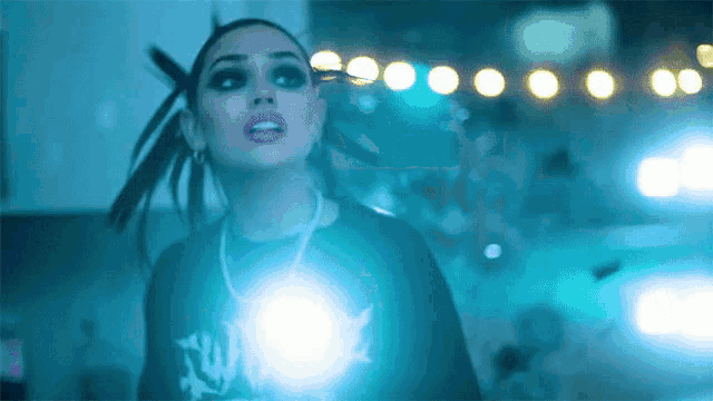 a woman in a black shirt with the word all on it is standing in front of a blue light