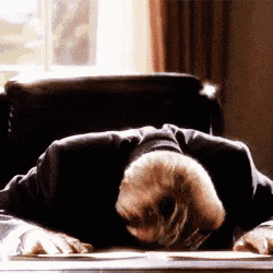 a man in a suit is laying on a desk with his head down .