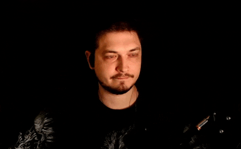 a man with a beard is wearing headphones and waving his hand in the dark .