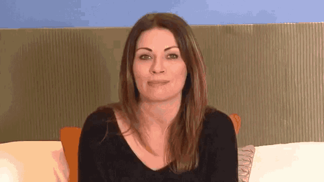 a woman in a black shirt is sitting on a couch with a pillow and making a funny face .