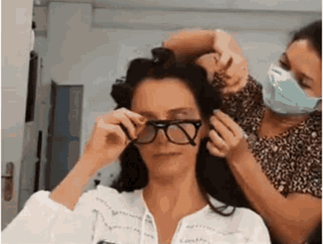 a woman is wearing glasses and getting her hair done by a hairdresser .