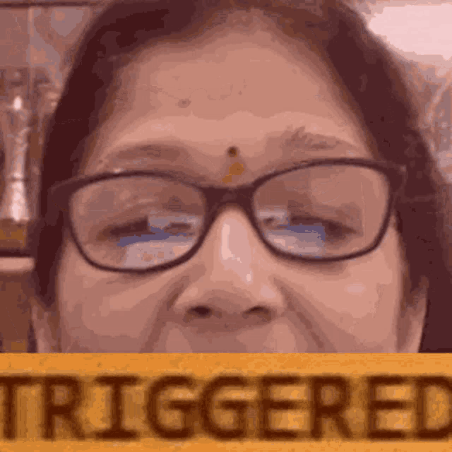 a close up of a woman wearing glasses and holding a sign that says triggered .