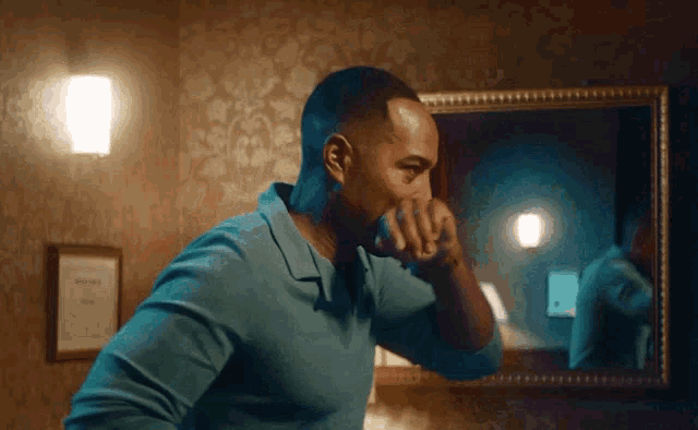 a man in a blue shirt looks at himself in the mirror