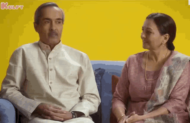 a man and a woman are sitting on a couch and the letters kulfy are on the bottom right