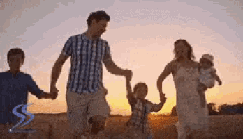 a family is walking in a field holding hands at sunset .