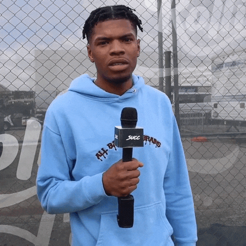 a man in a light blue hoodie holding a microphone that says sucl