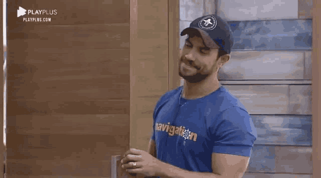 a man wearing a blue shirt that says navigation is standing in front of a wooden door .