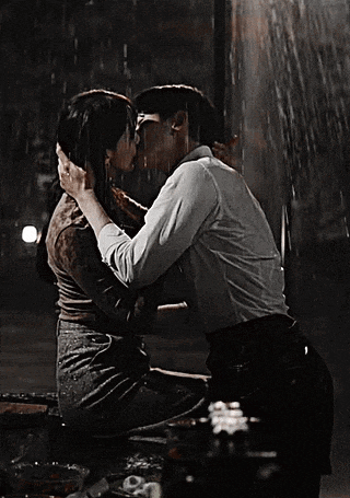 a man and woman kissing in the rain while sitting on a bench