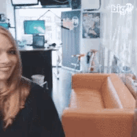 a woman is smiling in a room with a couch and a computer