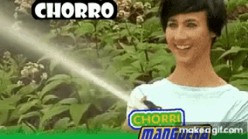 a woman is spraying a plant with a water hose and smiling .