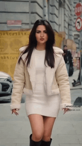 a woman in a white dress and white jacket is walking down the street