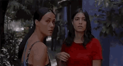 two women are standing next to each other on a sidewalk and talking .