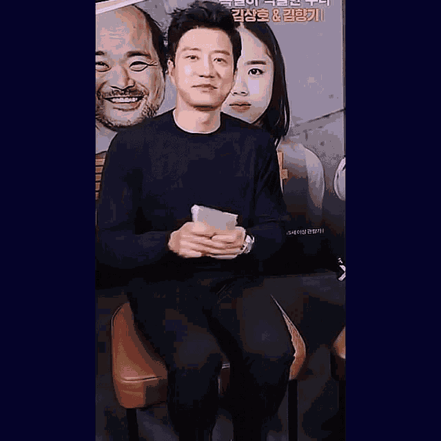 a man in a black shirt is sitting in front of a sign that says ' korean ' on it