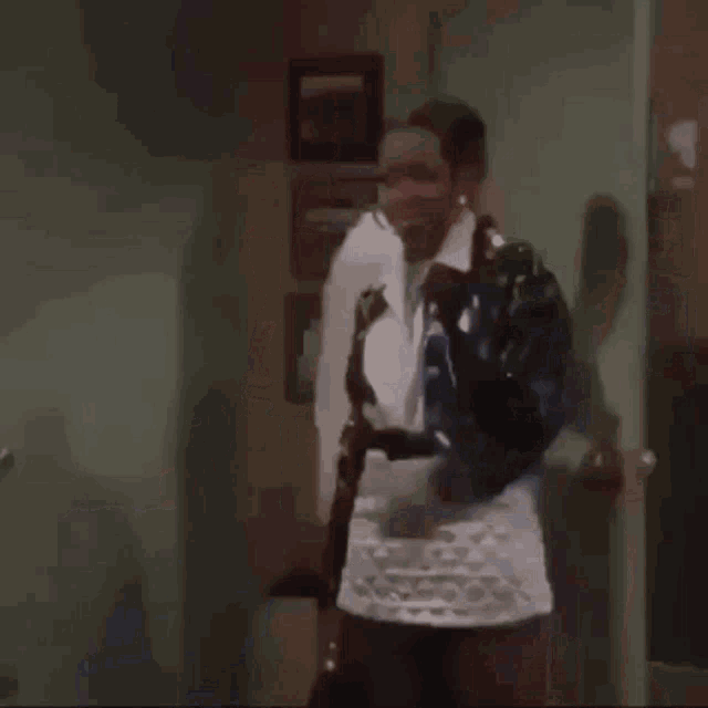 a woman in a white skirt and a black jacket is dancing in a room while a man stands behind her .