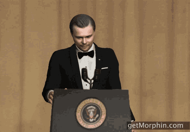 a man in a tuxedo stands behind a podium with the seal of the president of the united states of america on it