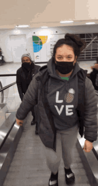 a woman wearing a mask and a sweatshirt that says love is walking down an escalator