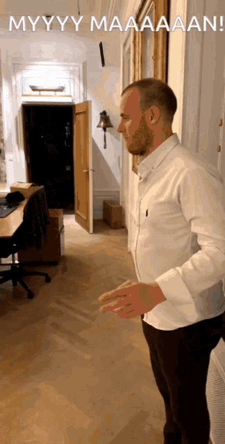 a man in a white shirt is standing in a hallway with the words myyyy maaaaan on the bottom