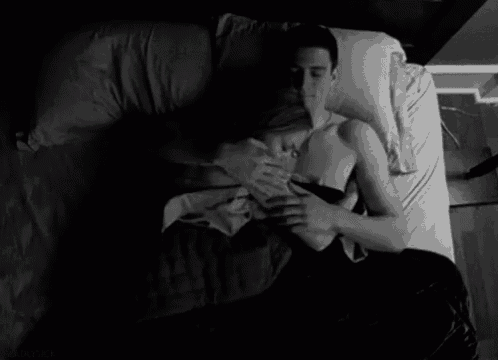 a man and a woman are laying on a bed and the man is touching the woman 's breast .