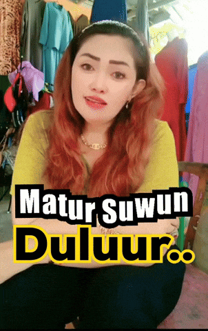a woman with red hair is sitting in front of a sign that says matur suwun duluur