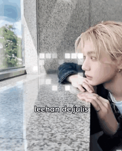 a young man is sitting at a table looking out a window and says lechan de julis .