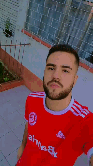 a man in a red adidas shirt holds a can of soda