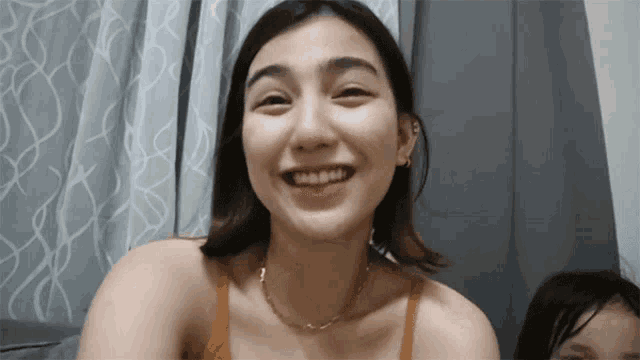 a woman wearing a necklace smiles while sitting on a couch