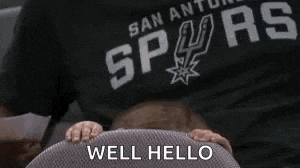 a man wearing a san antonio spurs shirt is sitting in a chair with his hands on the seat .