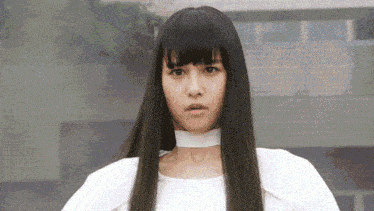 a woman with long black hair and a white choker is standing in front of a building and making a funny face .