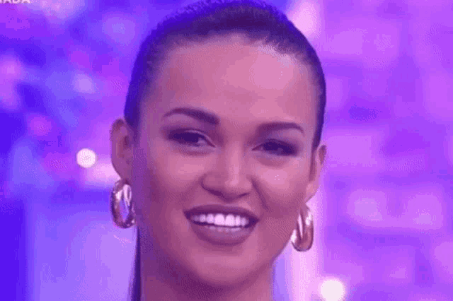 a close up of a woman wearing hoop earrings and a ponytail on a purple background .
