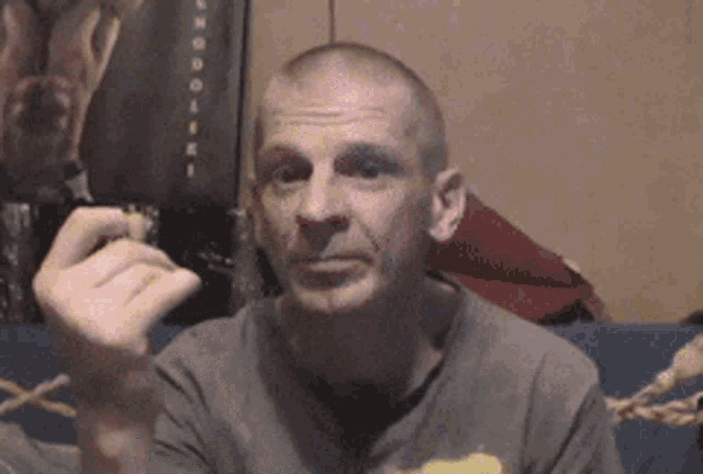 a man with a shaved head is sitting on a couch eating a sandwich