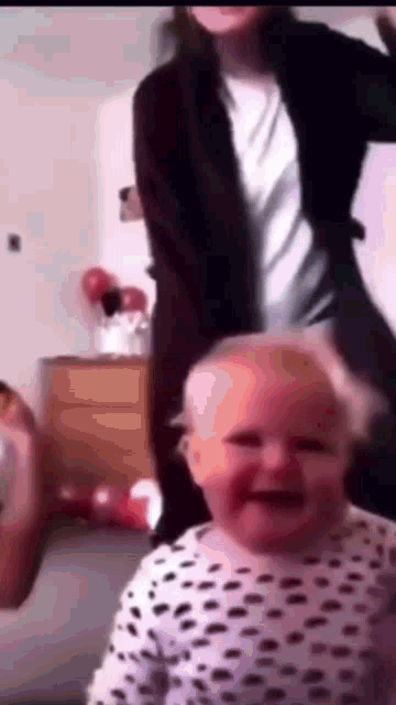 a baby in a dalmatian print shirt is laughing while a woman stands behind it .