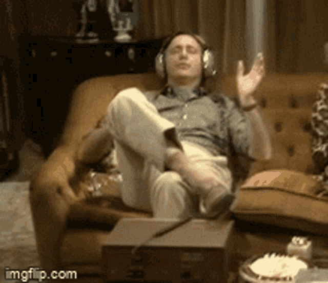 a man wearing headphones sits on a couch with his feet up