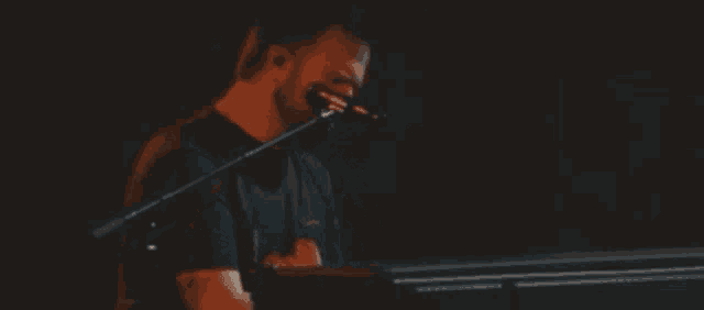 a man with a beard is playing a piano and singing into a microphone .