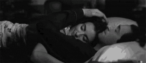 a black and white photo of a man and woman hugging each other while sleeping on a bed .