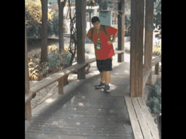 a man in a red shirt and black shorts is standing on a wooden bridge