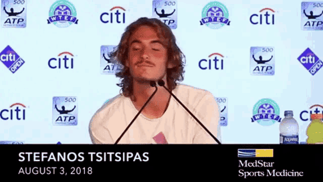 a man stands in front of a microphone with citi logos behind him