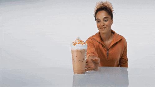 a woman is standing next to a cup of coffee with whipped cream and caramel sprinkles
