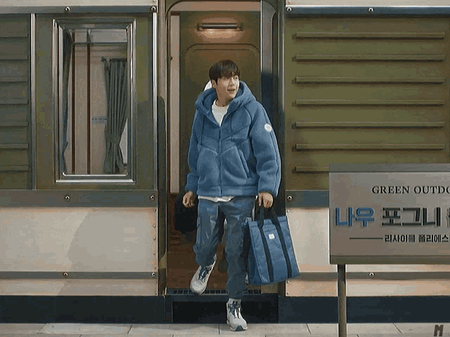 a man in a blue jacket is walking out of a building with a sign that says green outdoor