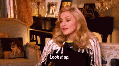 a woman is sitting on a couch in a living room and saying `` look it up '' .