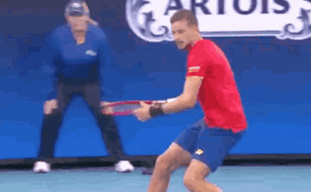 a man in a red shirt and blue shorts is holding a tennis racquet .