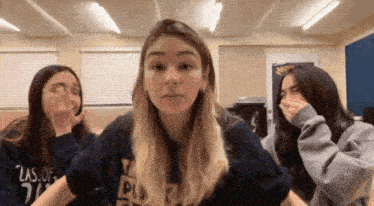 three girls are making funny faces in a room . one of the girls is wearing a shirt that says las of 21 .