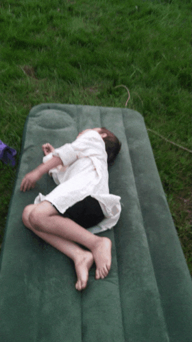 a young boy is laying on a green mattress in the grass