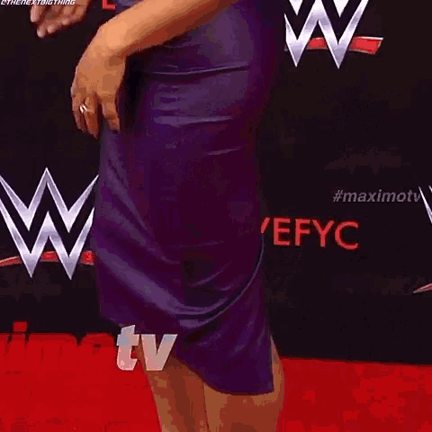 a woman with purple hair is standing in front of a wall that says wwefyc