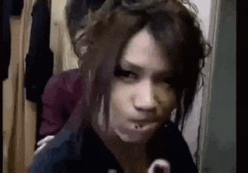 a woman with long hair and a piercing in her mouth is making a funny face in a room .