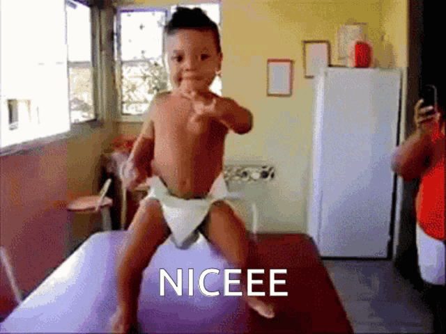 a baby in a diaper is pointing at the camera and the word niceee is on the bottom right
