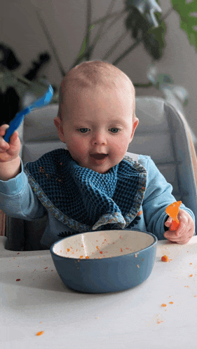 a baby wearing a bib is eating from a bowl with a spoon