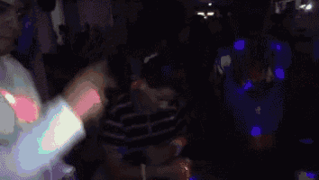 a group of people are dancing in a dark room while a man is holding a glass of water .