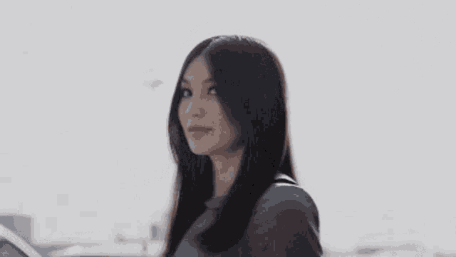 a woman with long hair is standing in front of a car and smiling .
