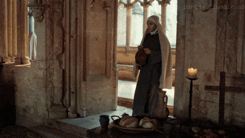 a nun stands in front of a table with bread and a candle in front of a window ..