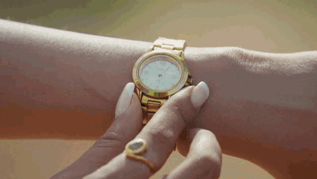 a woman wearing a gold watch on her wrist that says ' fossil ' on it